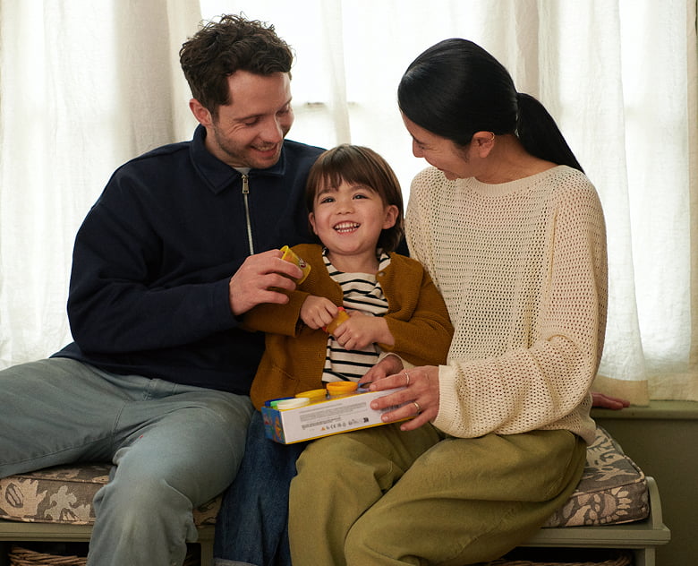 Photograph of a happy family of three sitting on a window seat playing together with a toy