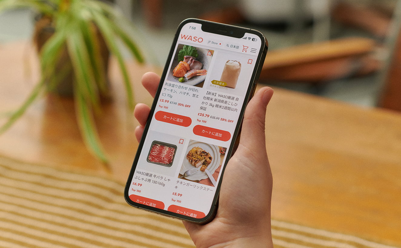 Photograph of a hand holding a smartphone displaying the WASO online store